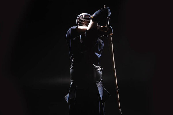 Боец Кендо в доспехах, практикующийся с бамбуковым мечом на черном
