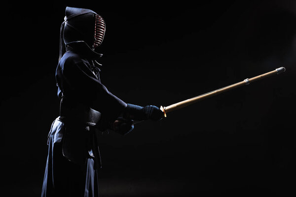 Боец Кендо в шлеме держит бамбуковый меч на черном
