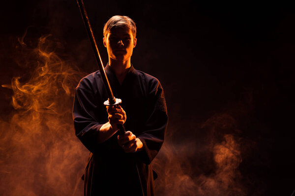 Молодой человек в кимоно держит меч Кендо в дыму
