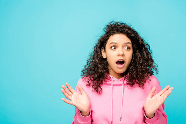 потрясенная кудрявая африканская американская девушка, стоящая изолированная на голубом
 