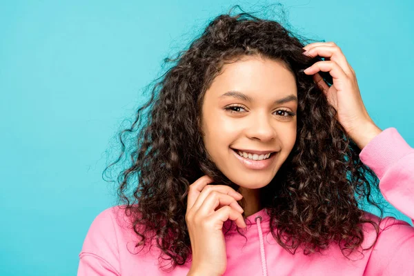Glimlachende Afro Amerikaanse Jonge Vrouw Aanraken Krullend Haar Geïsoleerd Blauw — Stockfoto