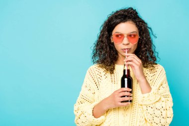 mavi üzerinde izole saman ve içme soda ile şişe tutan güneş gözlüğü kıvırcık Afrikalı Amerikalı kız