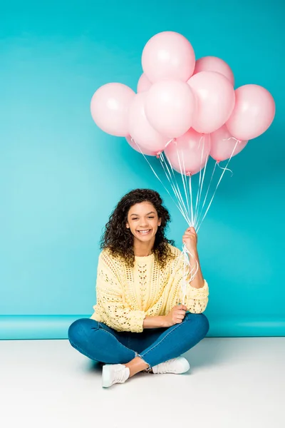 青の上にピンクのエア風船で座って幸せな巻き毛のアフリカ系アメリカ人の女の子 — ストック写真