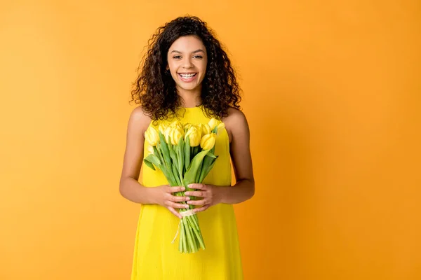 Alegre Encaracolado Afro Americano Mulher Segurando Tulipas Amarelas Isoladas Laranja — Fotografia de Stock