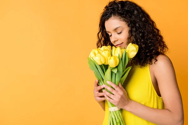 Atractiva Mujer Afroamericana Rizada Oliendo Tulipanes Amarillos Aislados Naranja — Foto de Stock