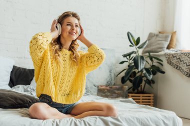 yatakta oturan ve evde müzik dinleme kulaklıklar güzel mutlu genç kadın