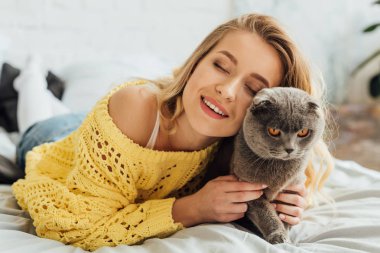gözler ile güzel gülümseyen kız yatak ve sarılma İskoç kat kedi yatıyor kapalı 