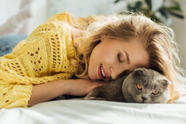 gözler ile güzel gülümseyen kız yatak ve sarılma İskoç kat kedi yatıyor kapalı 