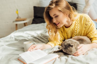 İskoç kat kedi ile yatakta yatarken güzel genç kadın kitap okuma 