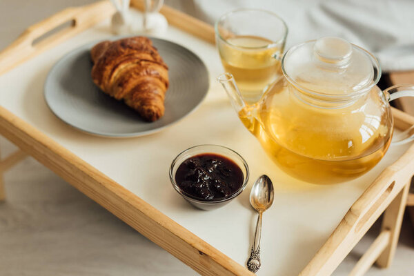 selective focus of wooden tray with croissant, jam, tea and tea pot