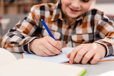 Ders sırasında defter yazılı damalı gömlek gülümseyen öğrenci kısmi görünümü