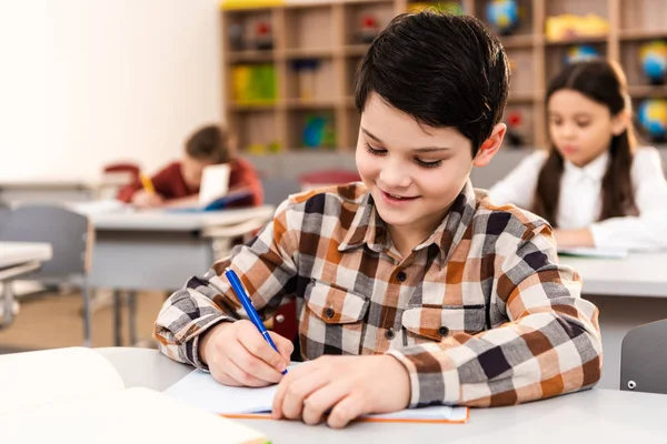 Pupila Morena Sonriente Con Camisa Cuadros Escribiendo Cuaderno Durante Lección — Foto de Stock