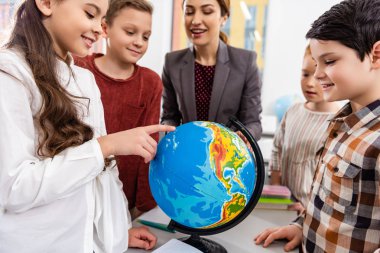Teacher and pupils looking at globe while studying geography in classroom clipart