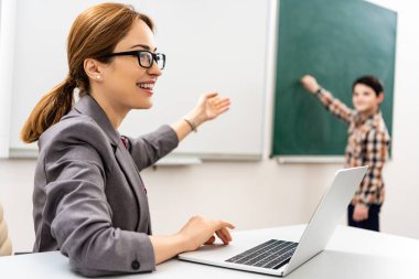 Dizüstü bilgisayar ile gözlük gülümseyen öğretmen tahta el ile işaret