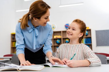 Sınıfta öğrenciye ders açıklayan mavi bluz öğretmen