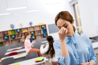 Masaların önünde duran mavi bluz ve burun dokunmadan yorgun öğretmen