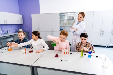 Pupils with flasks doing chemical experiment during chemistry lesson clipart