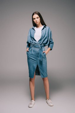 young adult and beautiful woman in denim dress with hands in pockets looking at camera clipart
