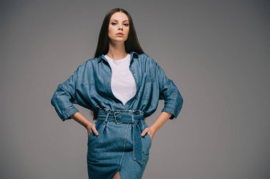 Kameraya bakarak kalça üzerinde elleriyle denim elbiseli esmer ve güzel kadın