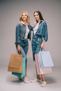 güzel sarışın ve esmer kadınlar alışveriş torbaları gri arka plan üzerinde tutarak denim giysileri 