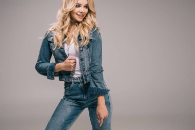 attractive blonde woman in denim jacket and jeans smiling and looking away  clipart