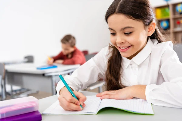 Colegiala Sonriente Escribiendo Cuaderno Durante Lección Aula —  Fotos de Stock