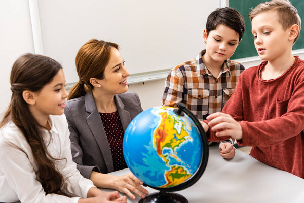 Teacher and pupils looking at globe while studying geography in classroom