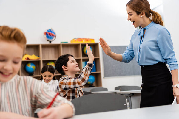 Smiling teacher and pupil raising hands for high five in classroom