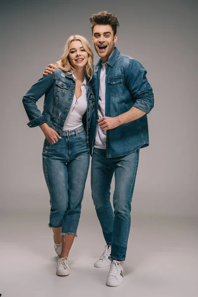 happy boyfriend and smiling girlfriend in denim clothes hugging and looking at camera