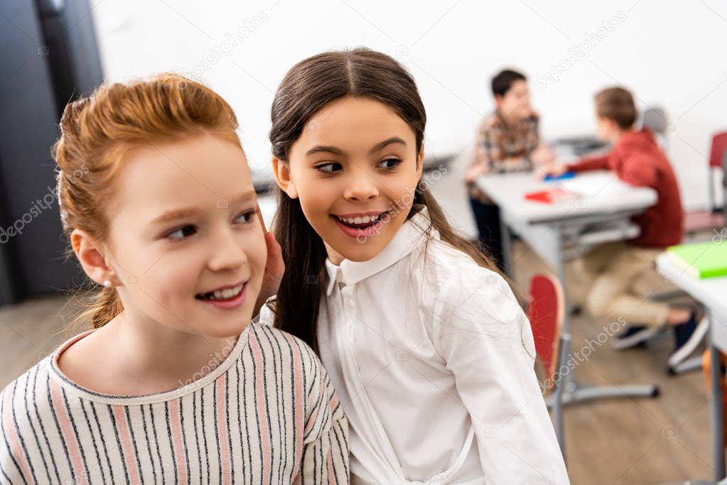 Two cute schoolgirls smiling and looking away in classroom during brake