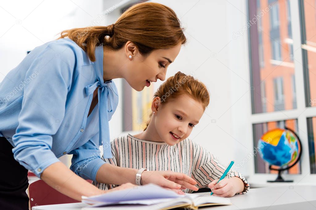 Teacher in blue blouse explaining lesson to pupil in classroom