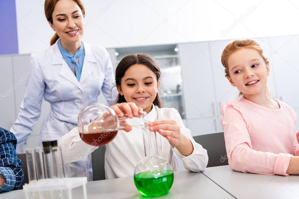 Smiling schoolgirl with beakers doing chemical experiment during chemistry lesson