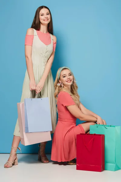 Morena Sonriente Mujeres Rubias Vestidos Sosteniendo Bolsas Compras Mirando Cámara —  Fotos de Stock