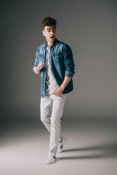 デニムのシャツとジーンズの灰色の背景を離れて驚くハンサムな男 — ストック写真