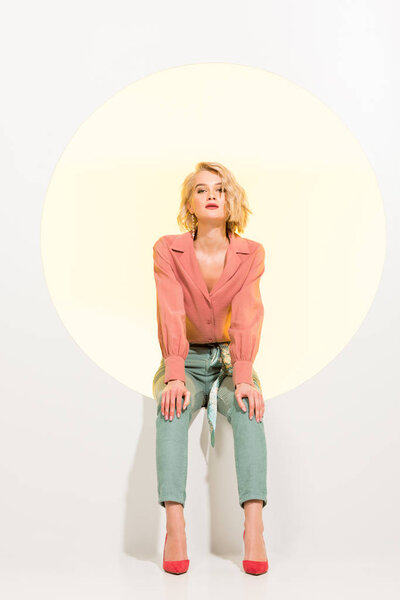 beautiful stylish girl looking at camera and posing while sitting on yellow circle with white background