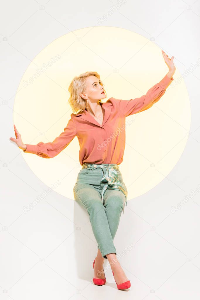 beautiful stylish girl posing while sitting on yellow circle with white background