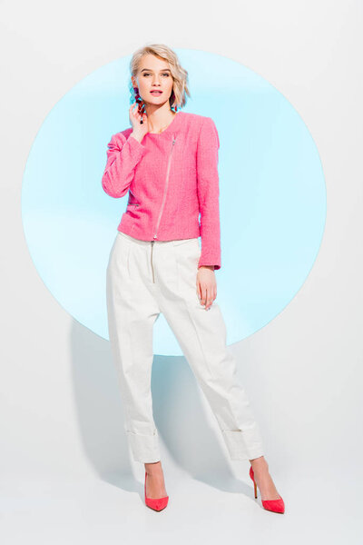 красивая стильная блондинка смотрит в камеру и позирует на белом с голубым кругом
