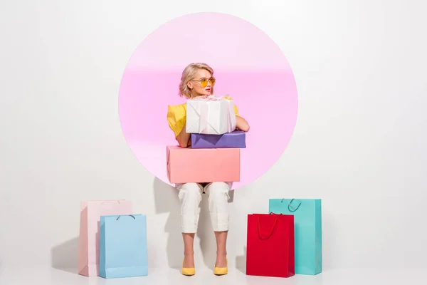 美丽的时尚女孩摆姿势与五颜六色的礼品盒和购物袋白色与粉红色的圆圈 — 图库照片