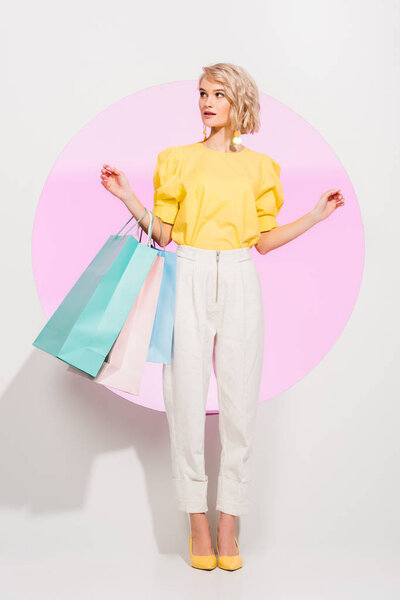 beautiful stylish girl holding colorful shopping bags and posing on white with pink circle