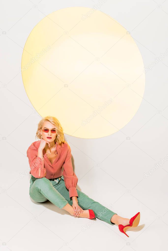 beautiful stylish girl in colorful clothes and sunglasses posing on white with yellow circle 