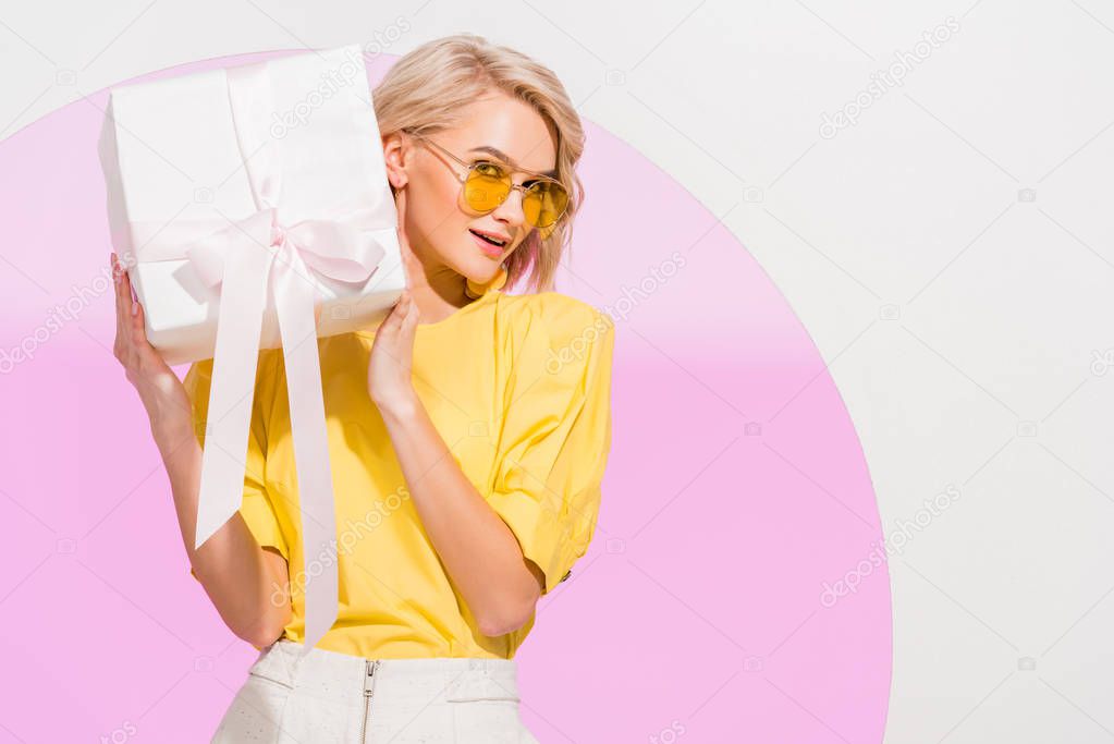 beautiful stylish girl looking at camera and holding gift box on white with pink circle