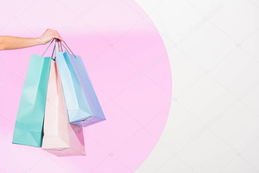 cropped view of young woman holding colorful shopping bags on white with pink circle