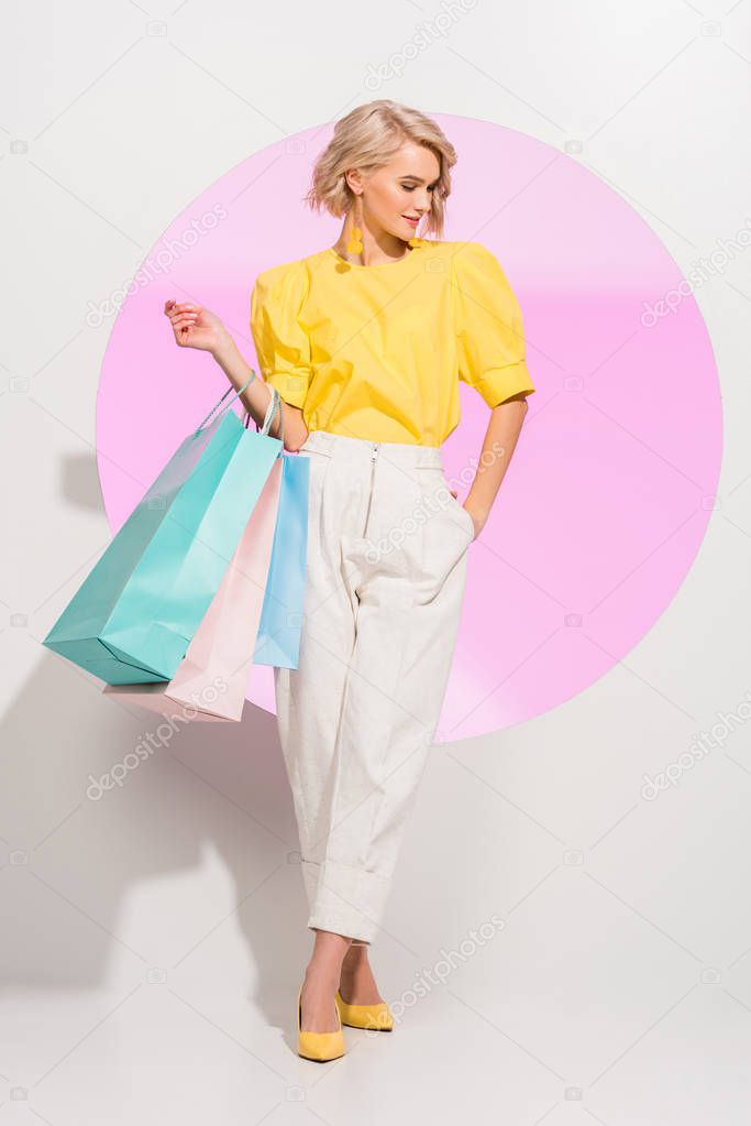 beautiful stylish girl holding colorful shopping bags and posing on white with pink circle