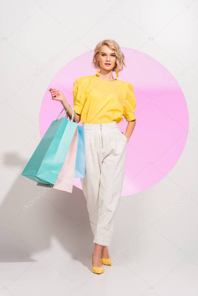 beautiful stylish girl looking at camera and holding colorful shopping bags on white with pink circle