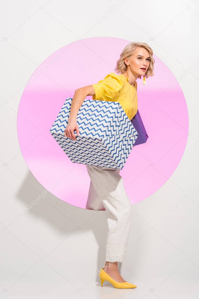 beautiful stylish young woman holding gift boxes and posing on white with pink circle