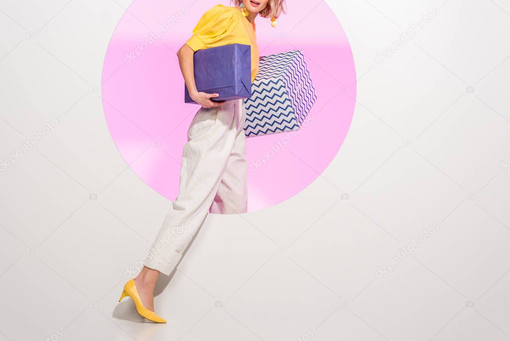 cropped view of stylish young woman holding gift boxes on white with pink circle and copy space