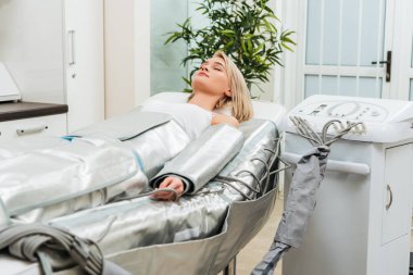 Sarışın kız Kapalı gözlerle pressotherapy oturumu sırasında klinikte yalan.