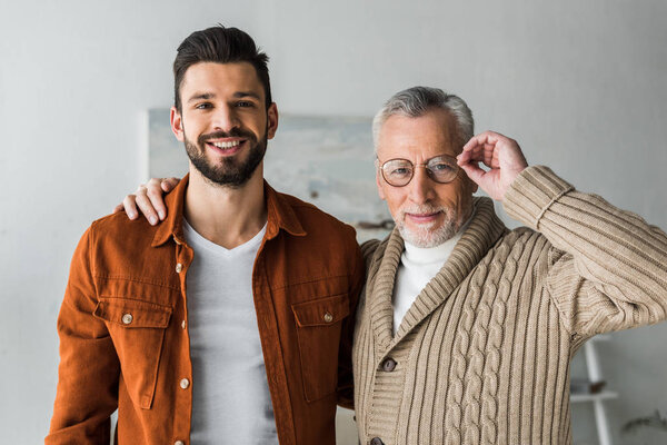Красивый мужчина улыбается, стоя с веселым старшим отцом трогательные очки
 