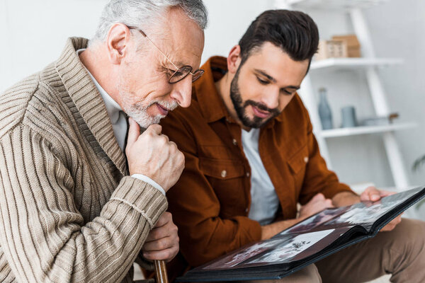 handsome bearded man and senior father in glasses looking at photo album 