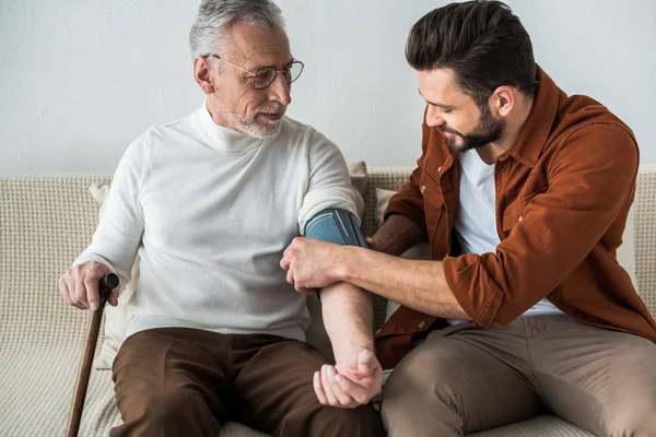 Skäggig Man Ler Medan Mäta Blodtryck Glad Senior Far Glas — Stockfoto